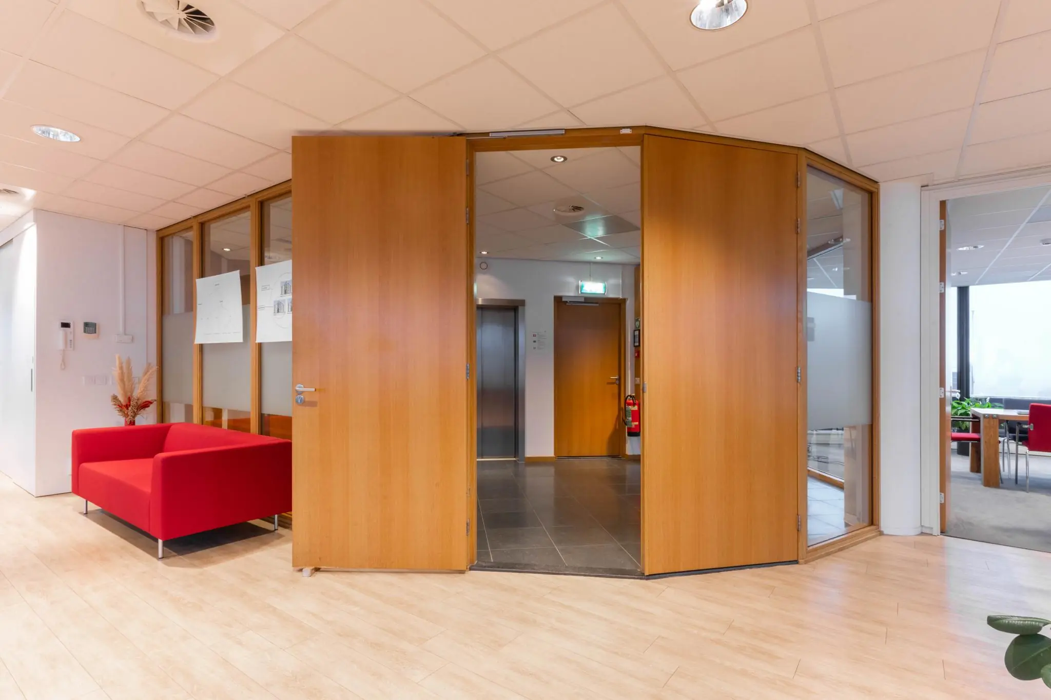 Ingang van een modern kantoor aan de 1e Hogeweg met houten deuren, rode zithoek en zicht op de lift.